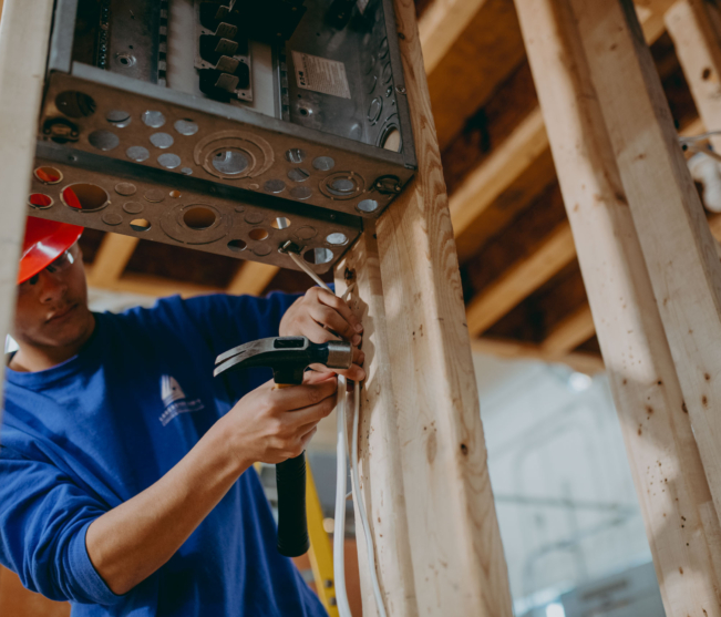 electrical student hammering wire along wood stud
