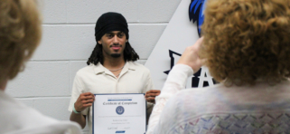 Welding student smiles at camera, holding certificate