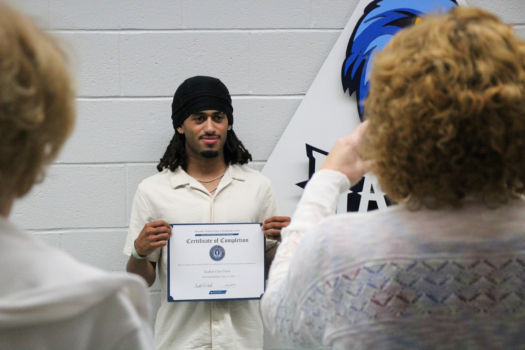 Welding student smiles at camera, holding certificate