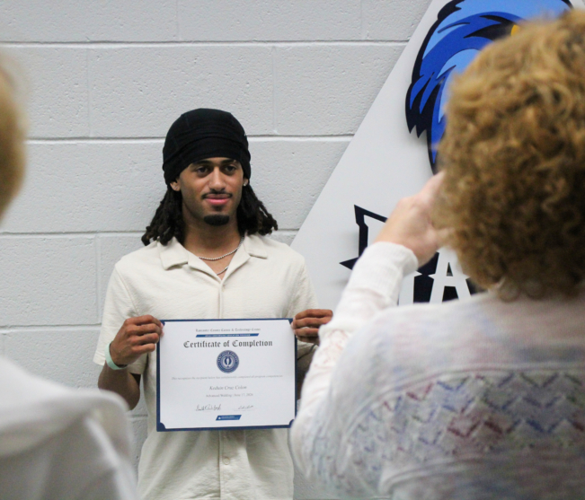 Welding student smiles at camera, holding certificate
